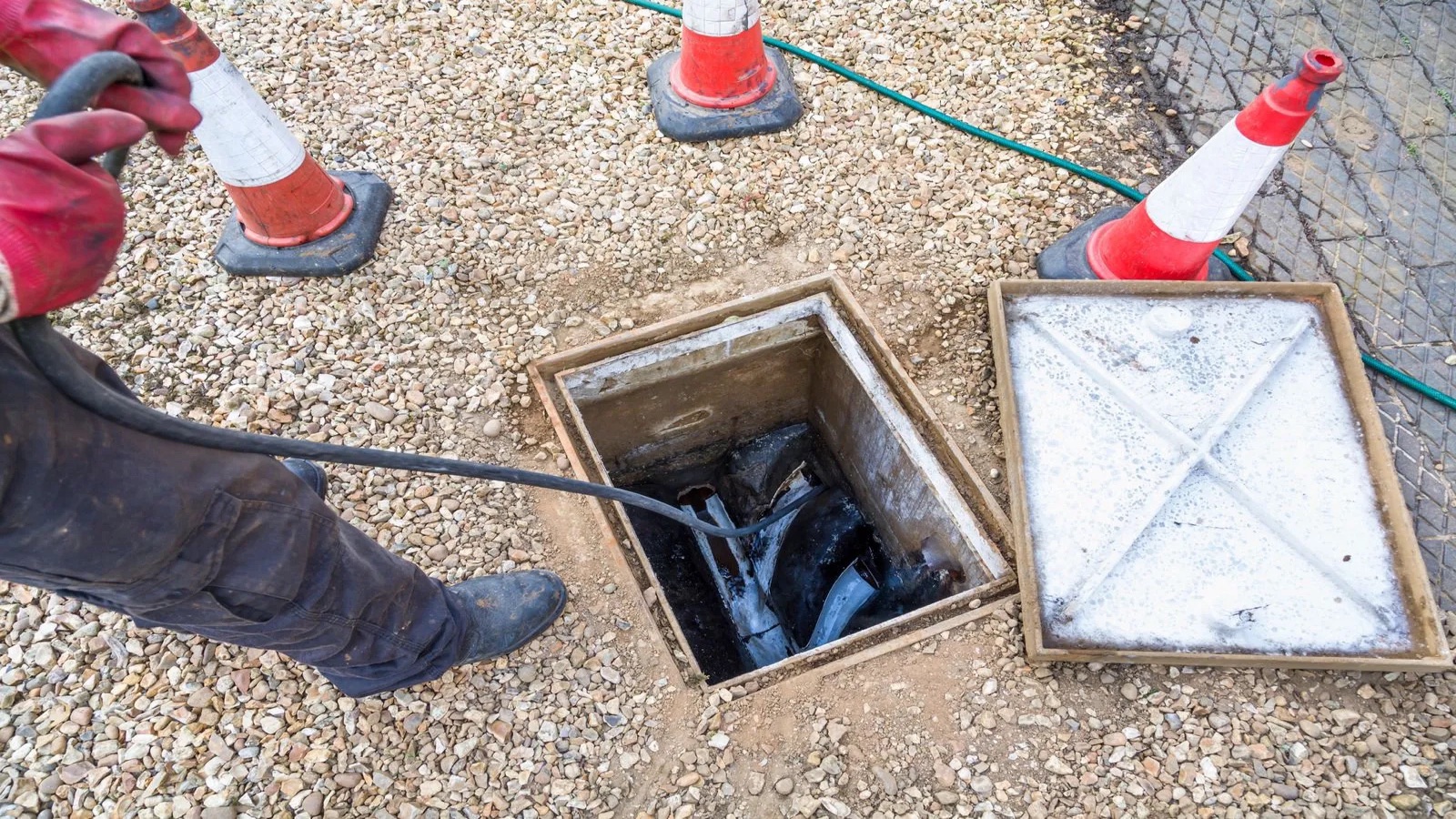 Technician cleaning an outdoor drain access with a high-pressure hose